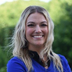 Mary, employee at Fox Crossing Chiropractic, headshot in front of a green nature background. Employee is smiling and wearing blue scrubs.